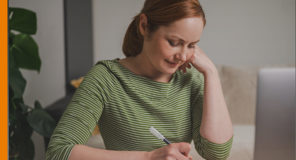 Woman reviewing financial documents at home while working on a laptop.