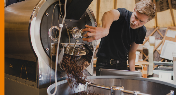 Small business owner operating coffee roasting machinery inside a specialist production workshop.